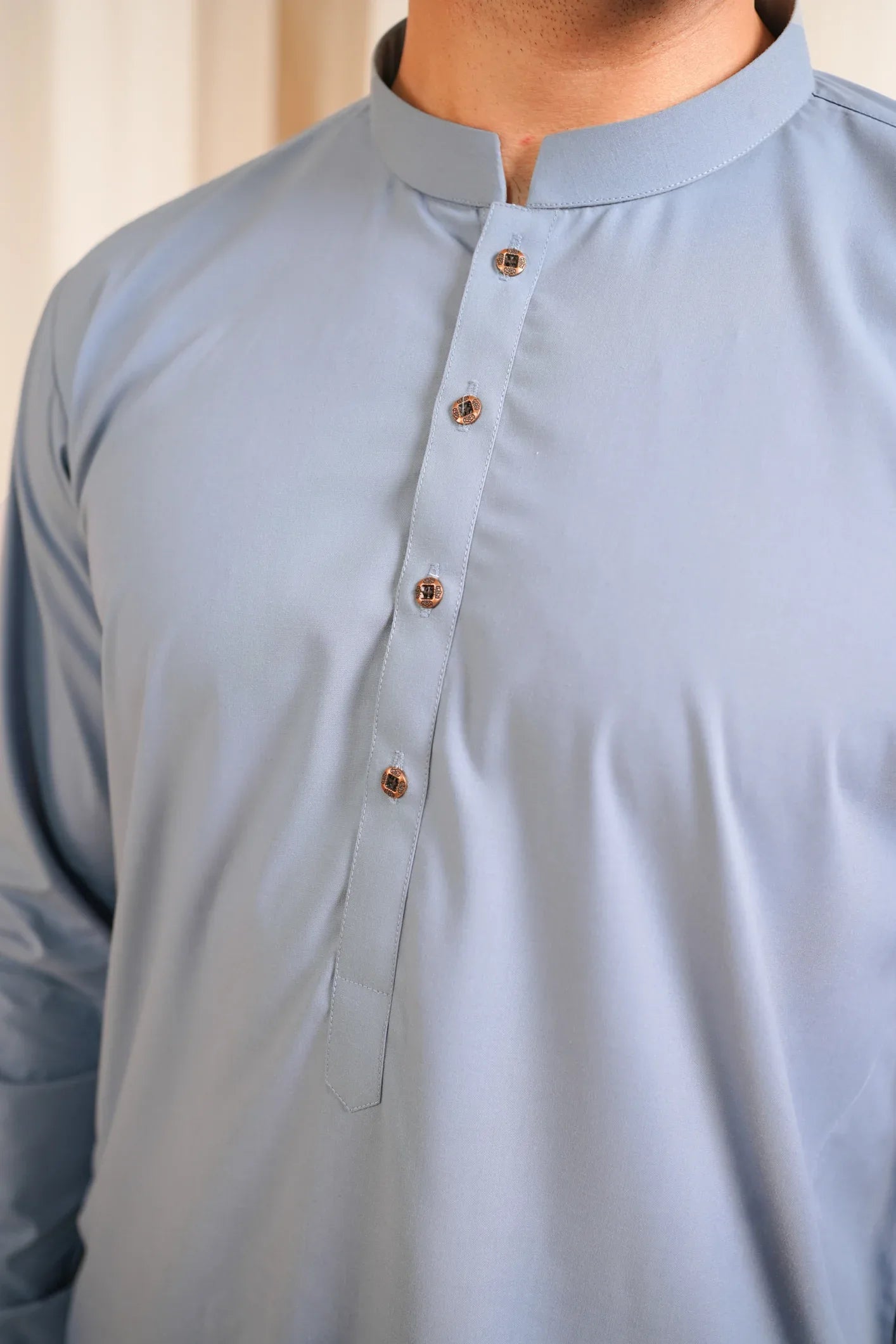 A man wearing a blue luxury blended kurta shalwar, standing against a curtain backdrop.