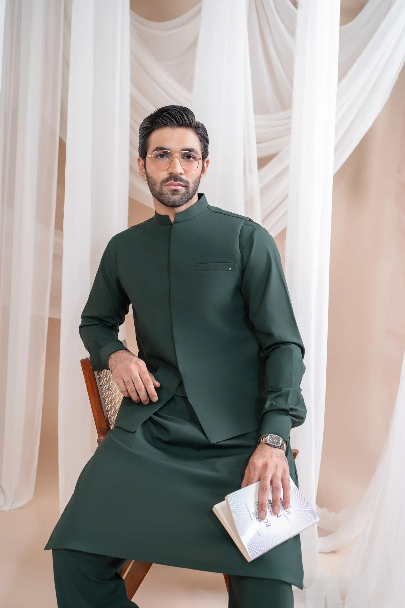 A man wearing a bottle green luxury formal Kameez Shalwar with a patch pocket waistcoat and full sleeves. The outfit is straight cut and suited for all-season wear.