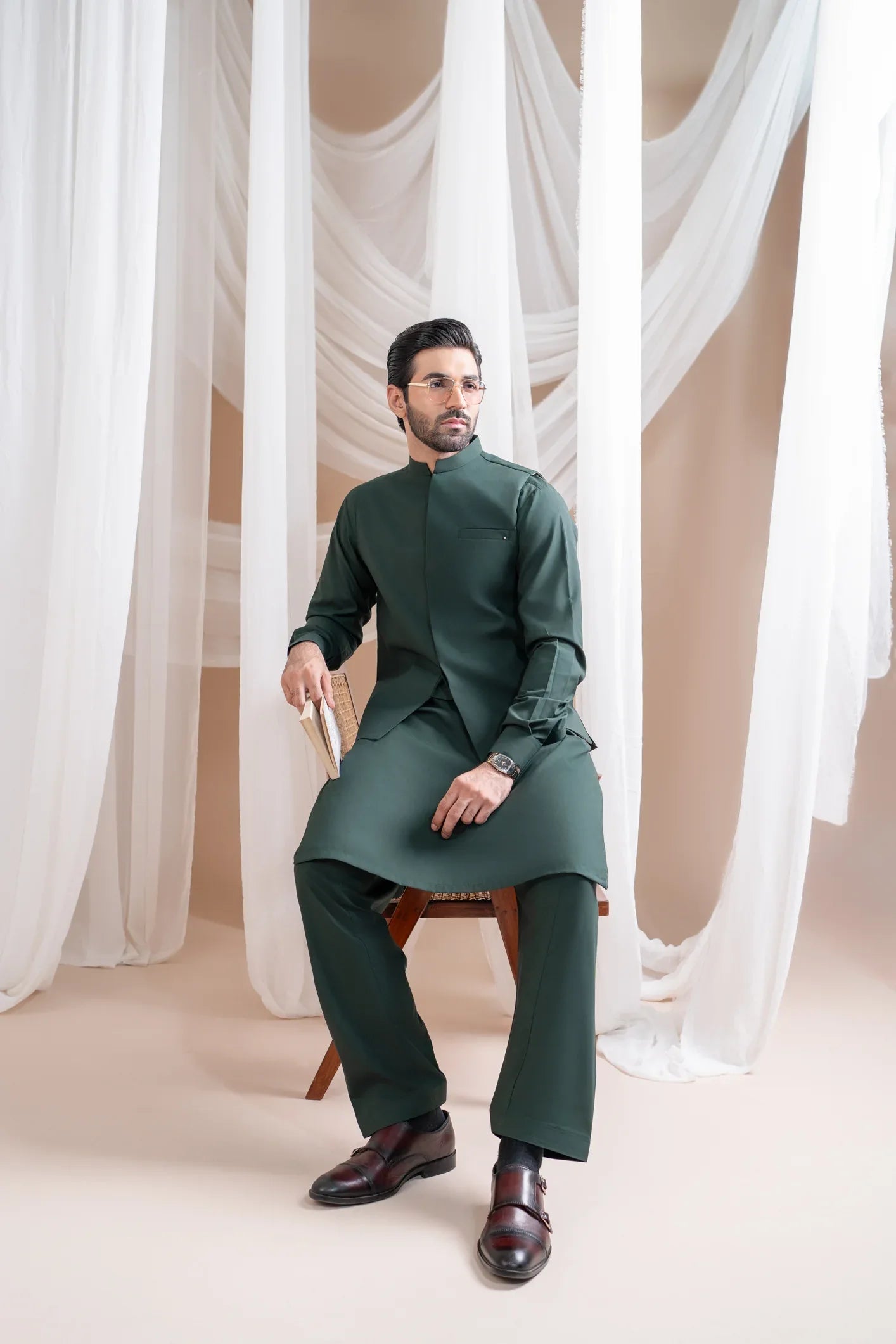 A man wearing a bottle green luxury formal Kameez Shalwar with a patch pocket waistcoat and full sleeves. The outfit is straight cut and suited for all-season wear.