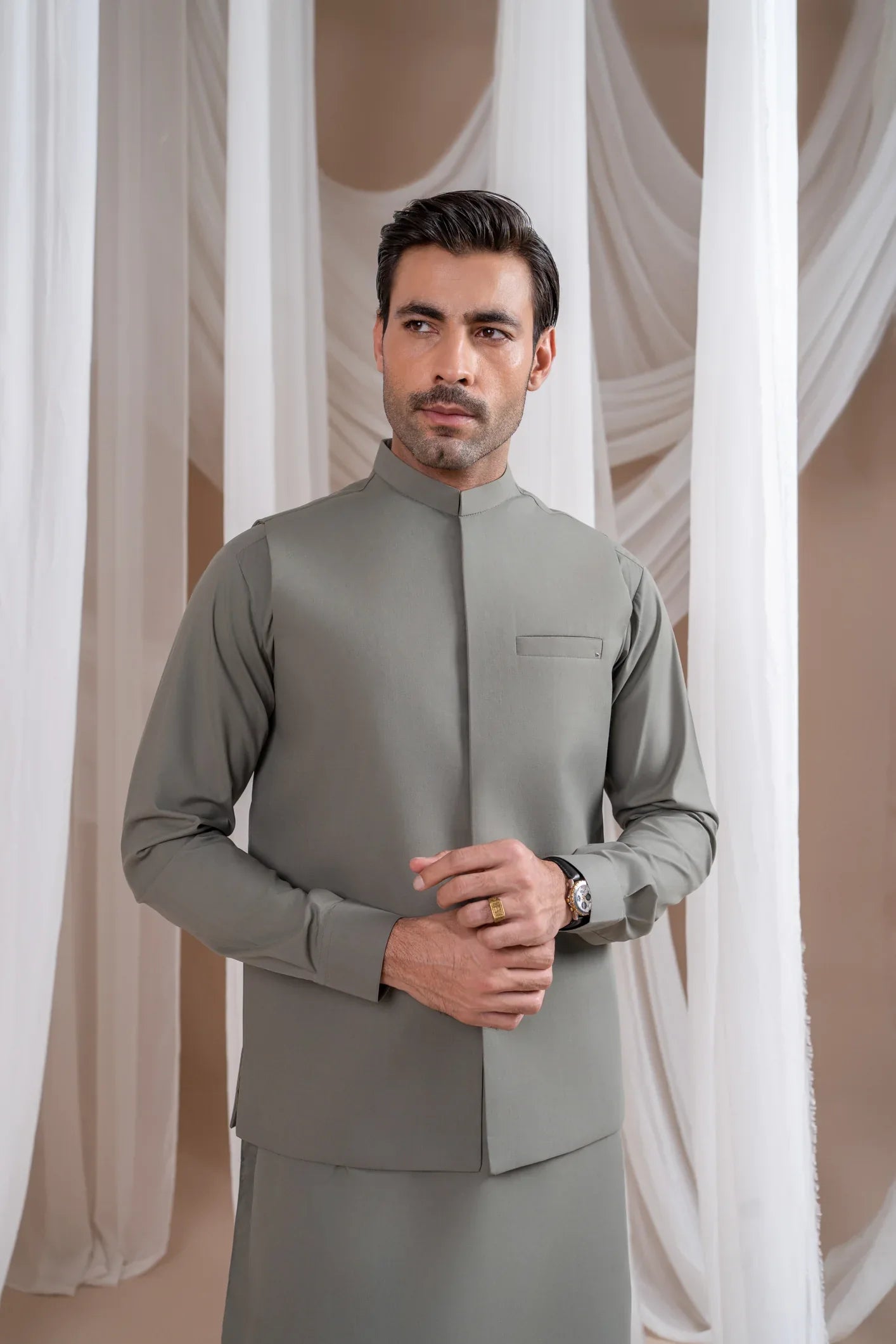 A man wearing a sand grey luxury formal Kameez Shalwar with a straight cut waistcoat and a patch pocket waistcoat.
