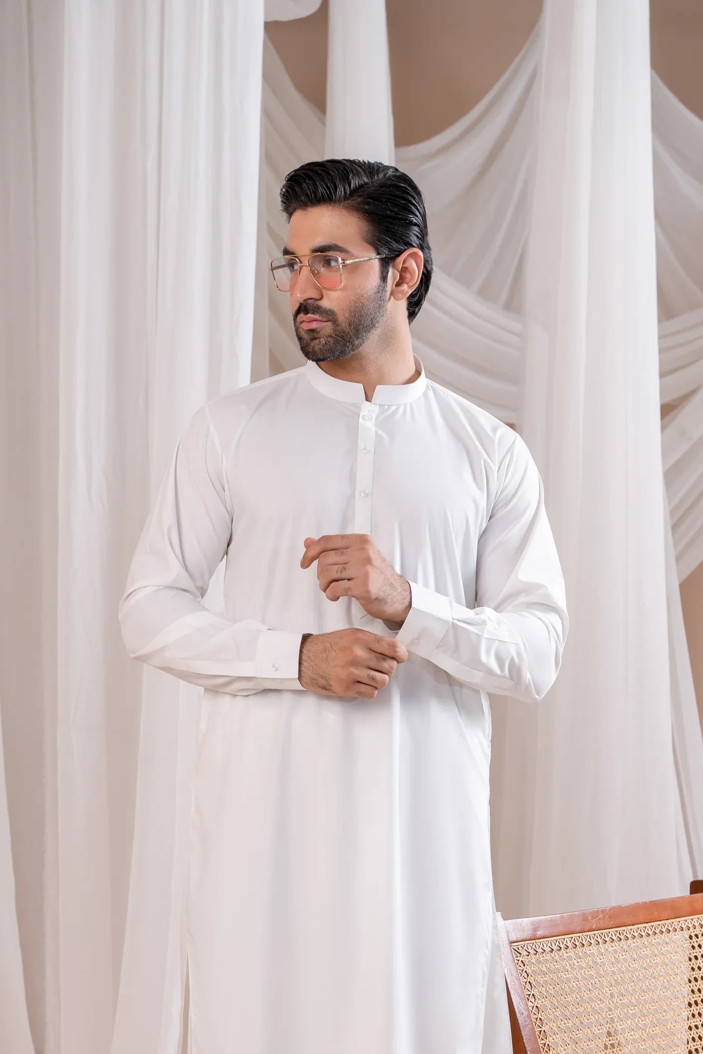A man standing in a white kameez shalwar with a mandarin collar, full sleeves, and a belt. The shalwar is displayed in an off-white color.