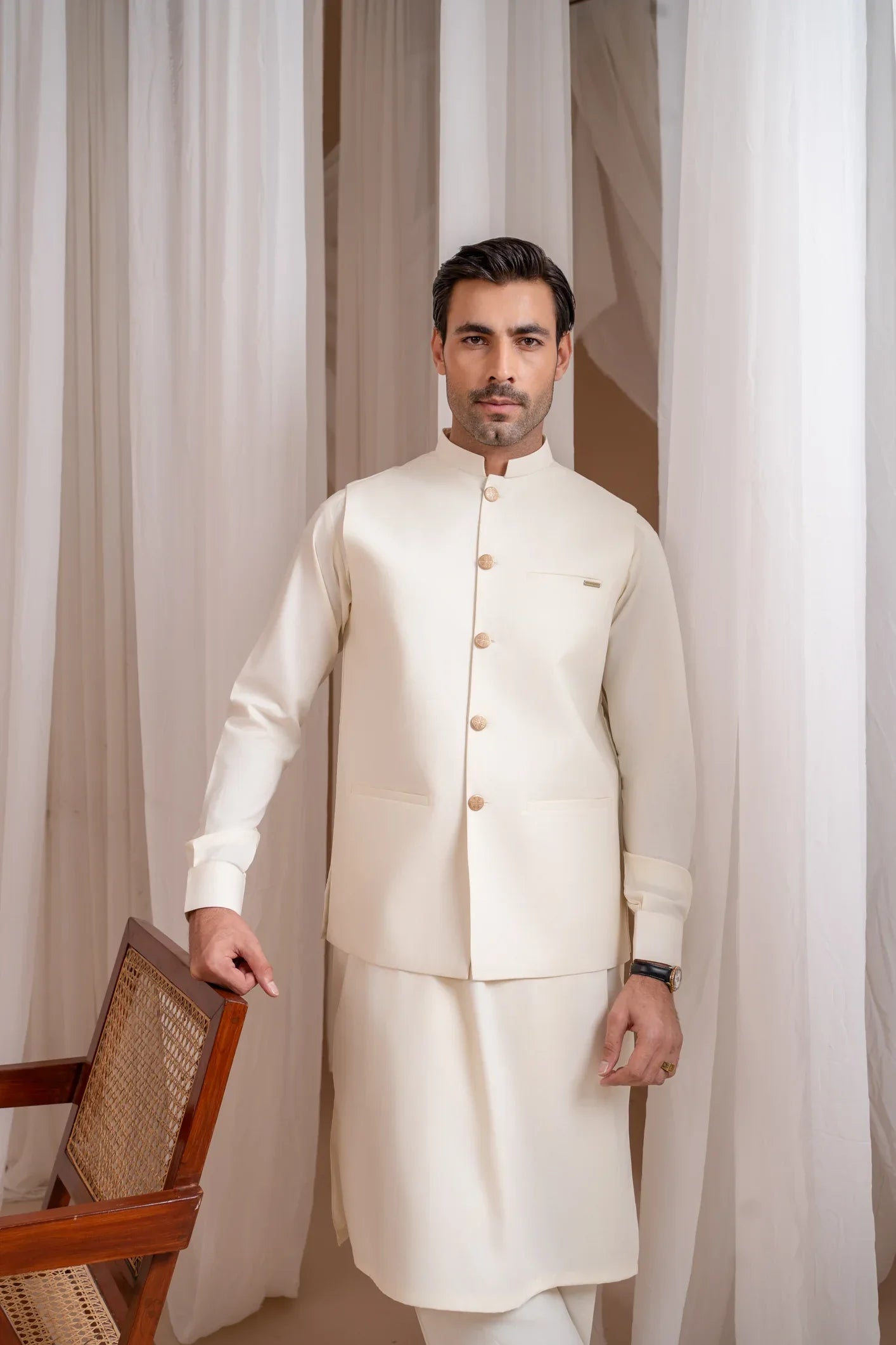 A man wearing a bosky white luxury formal kameez shalwar with a straight cut buttoned blended waistcoat.