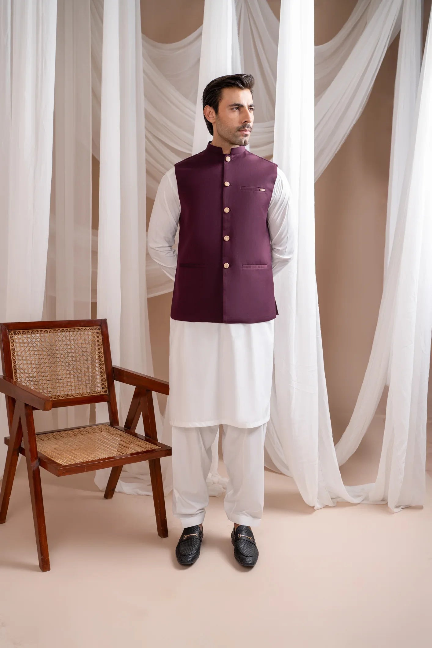 A man wearing a straight cut, buttoned, burgundy suiting waistcoat over a white shirt.
