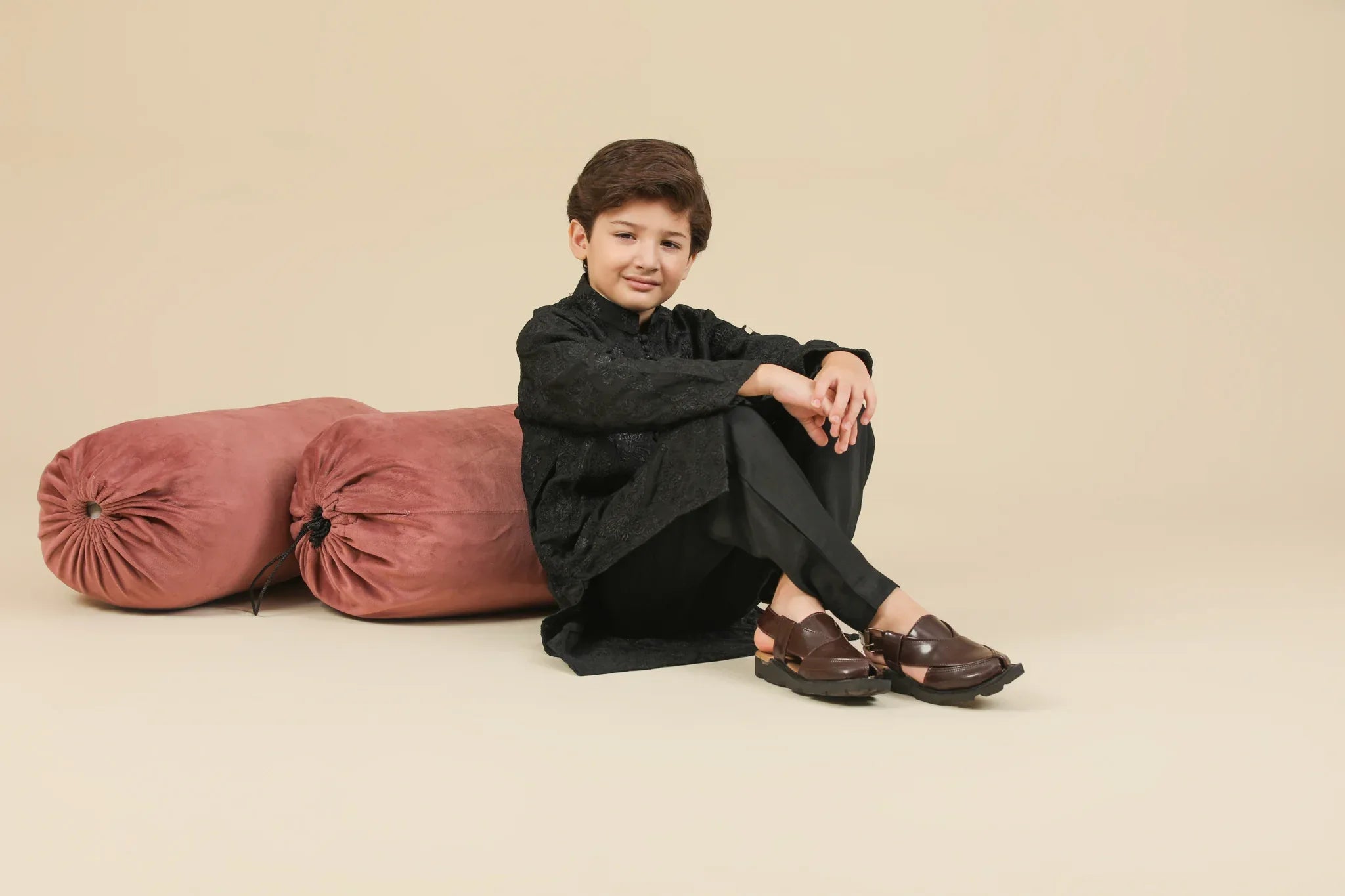 Young boy wearing a black raw silk embroidered kurta trouser outfit on a beige background