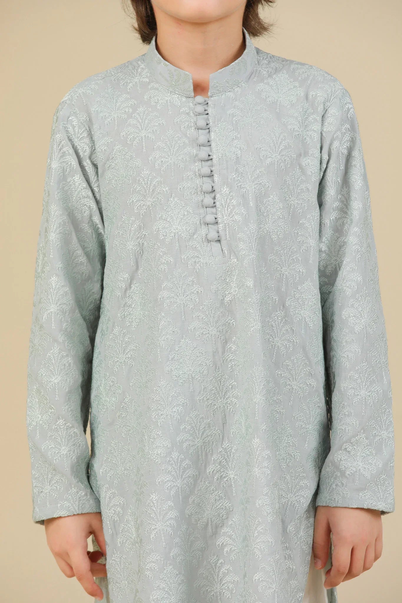 Young boy wearing an ice blue embroidered kurta with white pajama on a beige background