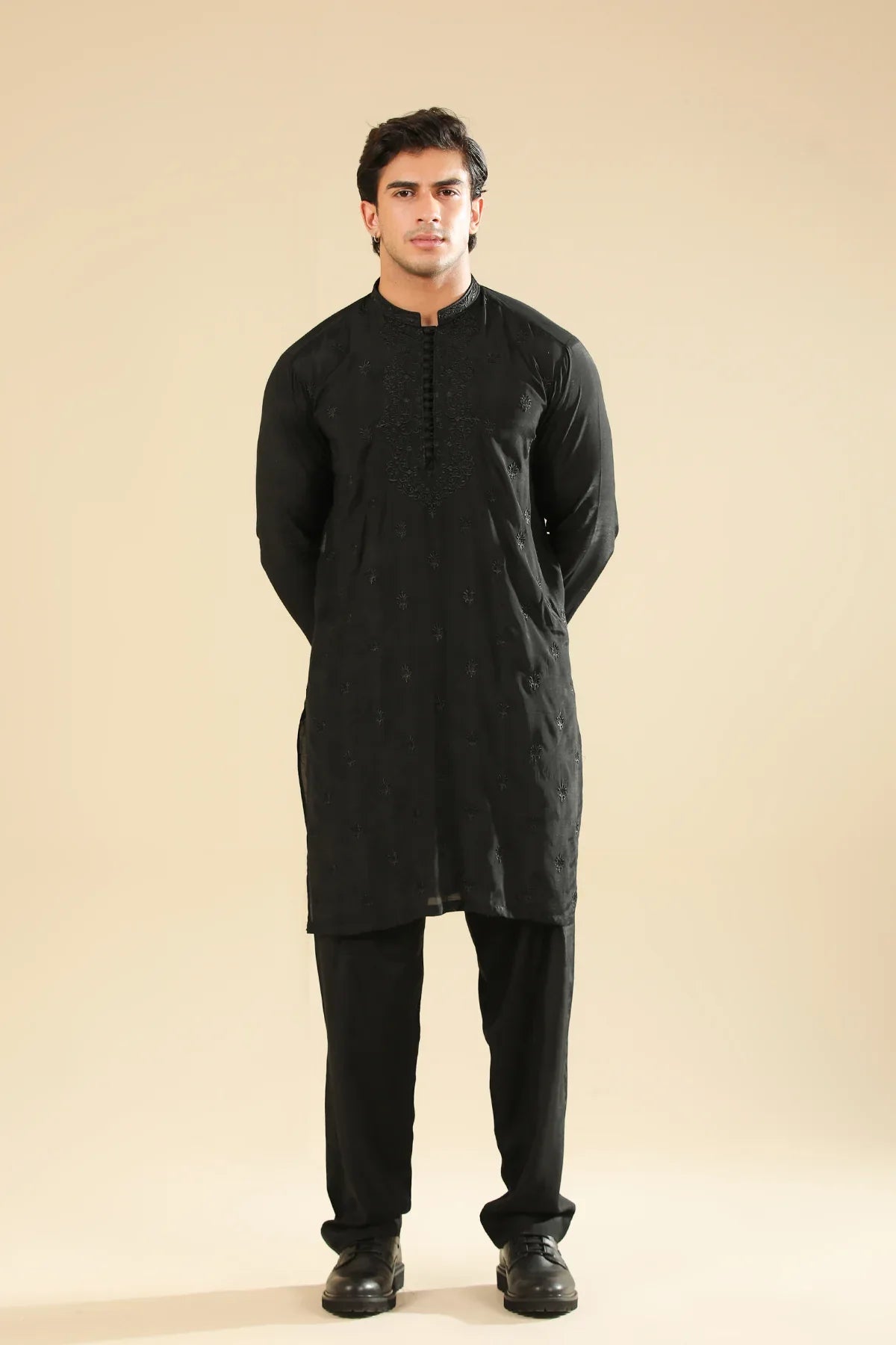 Man wearing a black raw silk embroidered kurta trouser against a beige background