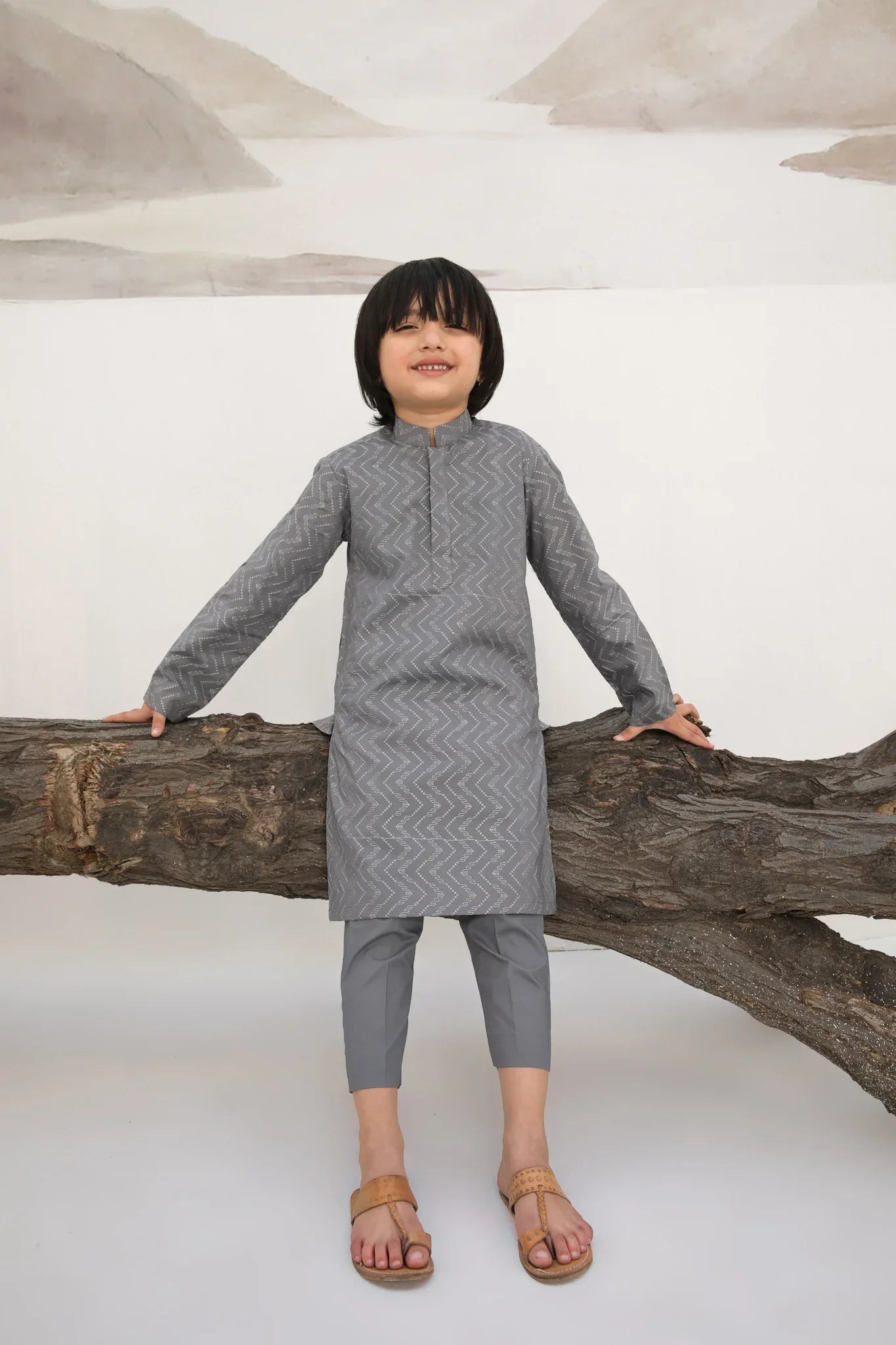 A child wearing a light grey embroidered kurta with a mandarin collar and full sleeves, paired with plain cotton trousers.