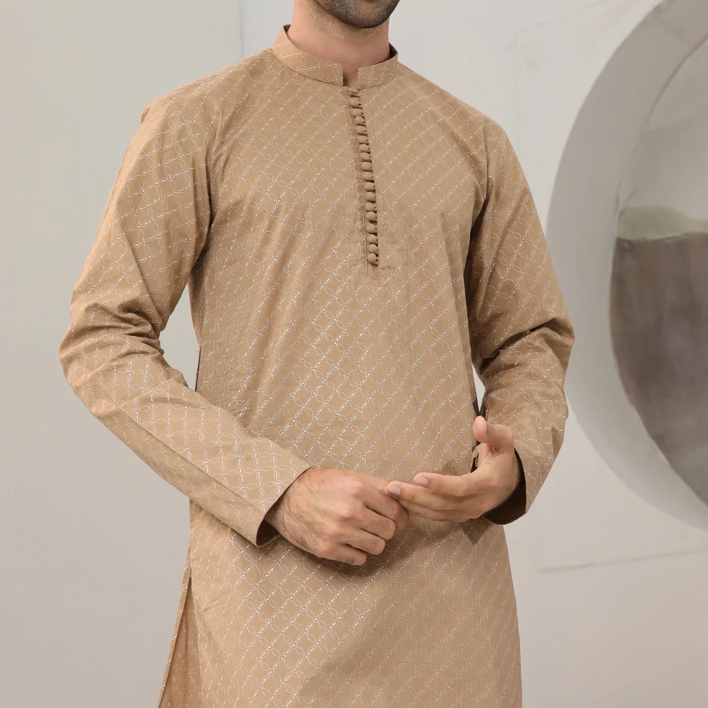 A man wearing a camel cotton embroidered kurta with full sleeves and a mandarin collar, paired with plain trousers.