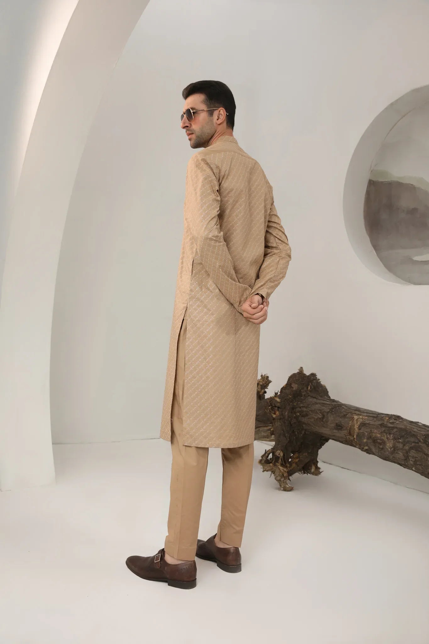 A man wearing a camel cotton embroidered kurta with full sleeves and a mandarin collar, paired with plain trousers.