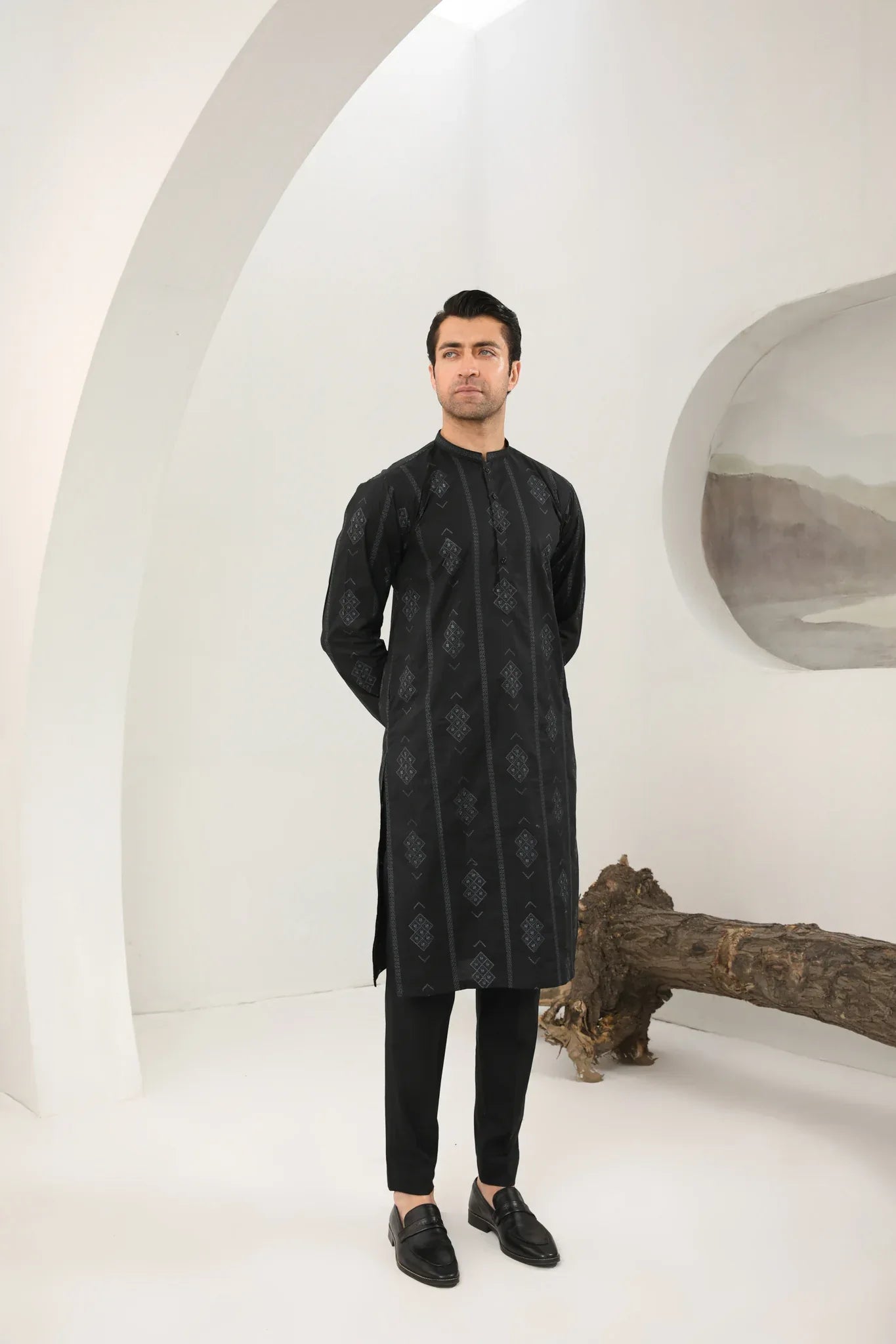 A man wearing a black embroidered kurta with full sleeves and a mandarin collar, paired with plain trousers.