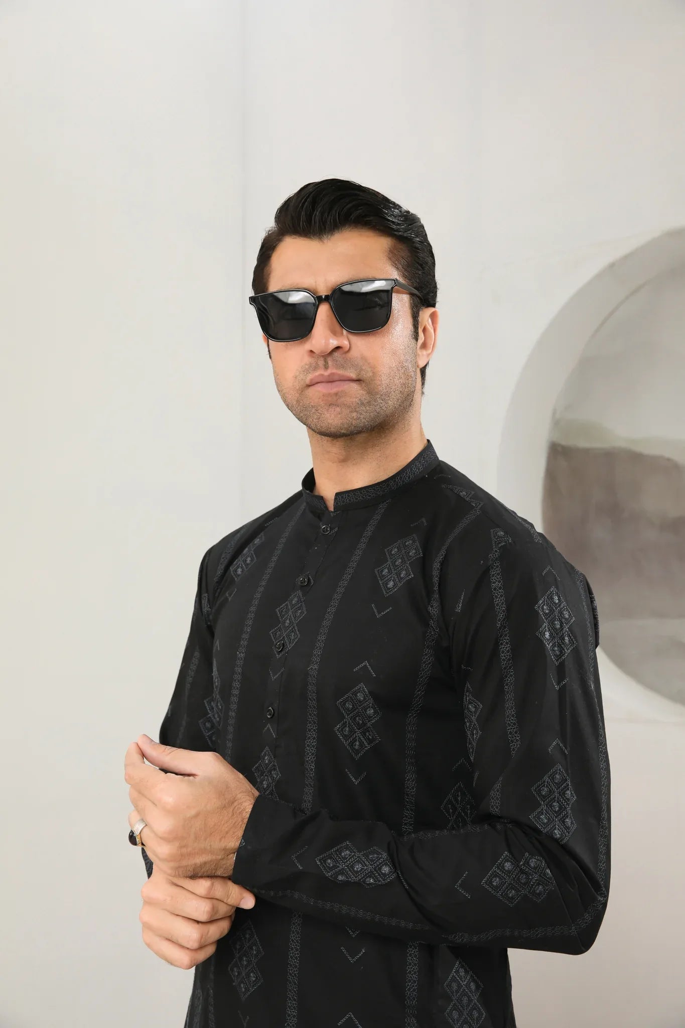 A man wearing a black embroidered kurta with full sleeves and a mandarin collar, paired with plain trousers.