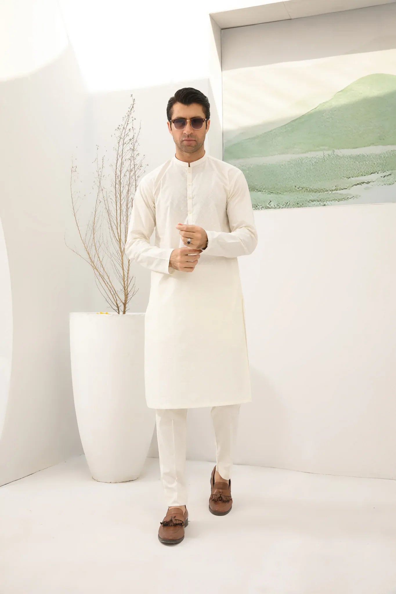 A man wearing a bsoky white cotton kurta embroidered with geometric patterns, featuring a mandarin collar and full sleeves, paired with plain trousers.