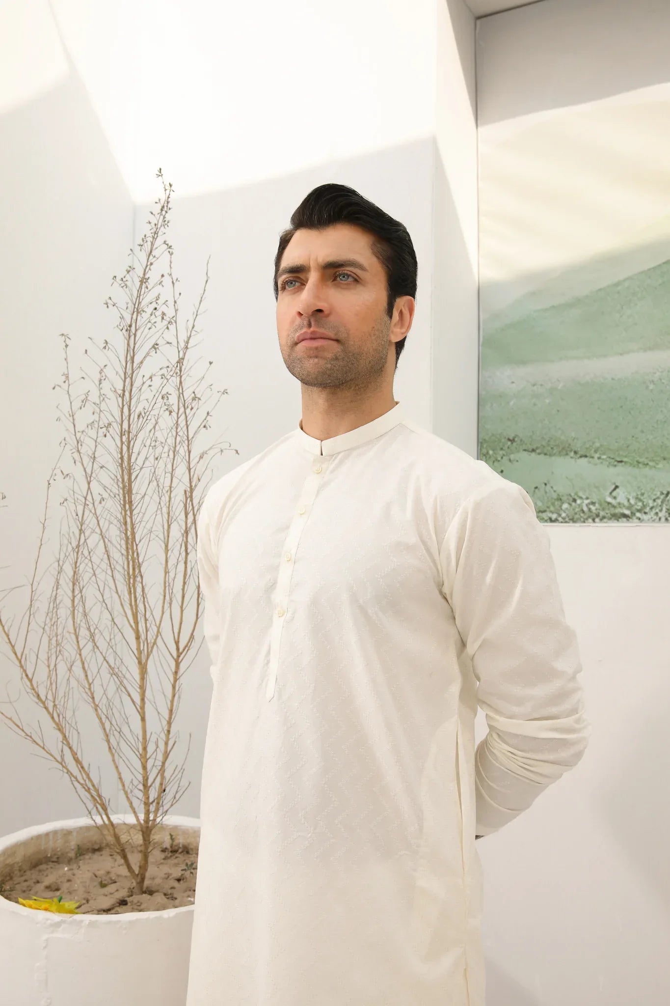 A man wearing a bsoky white cotton kurta embroidered with geometric patterns, featuring a mandarin collar and full sleeves, paired with plain trousers.