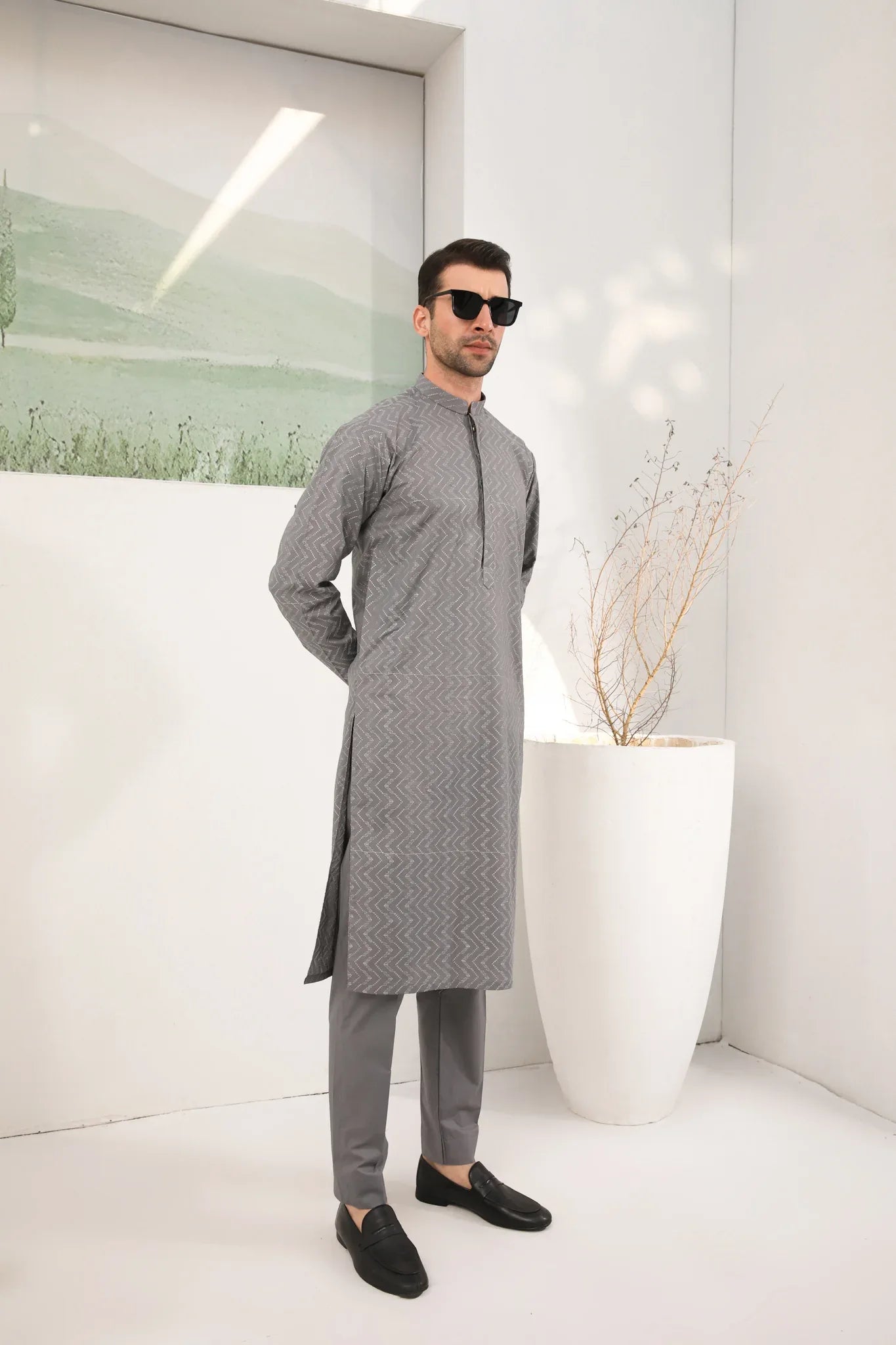 A man wearing a light grey embroidered kurta with full sleeves and a mandarin collar, paired with a plain trouser.