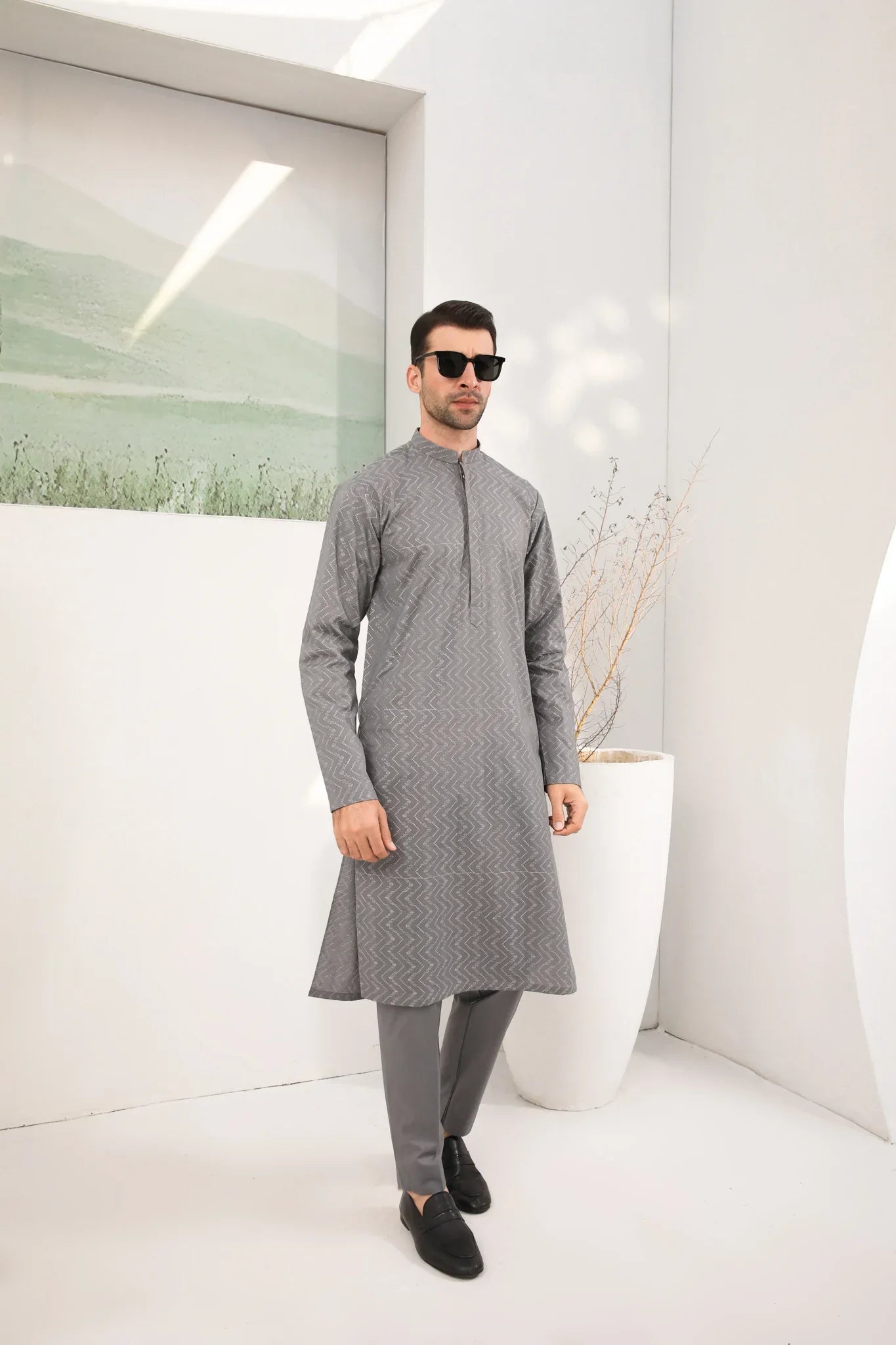 A man wearing a light grey embroidered kurta with full sleeves and a mandarin collar, paired with a plain trouser.