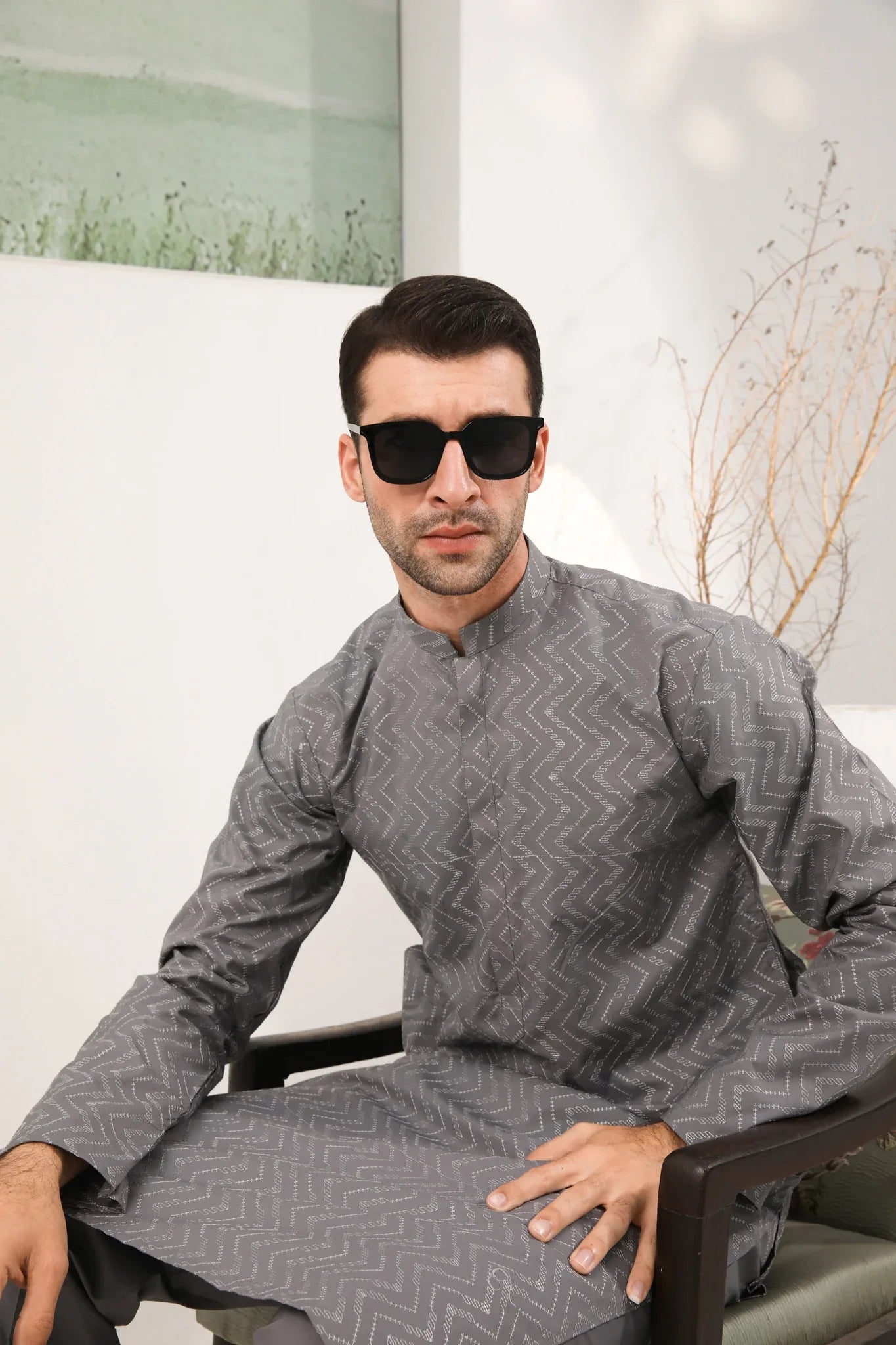 A man wearing a light grey embroidered kurta with full sleeves and a mandarin collar, paired with a plain trouser.