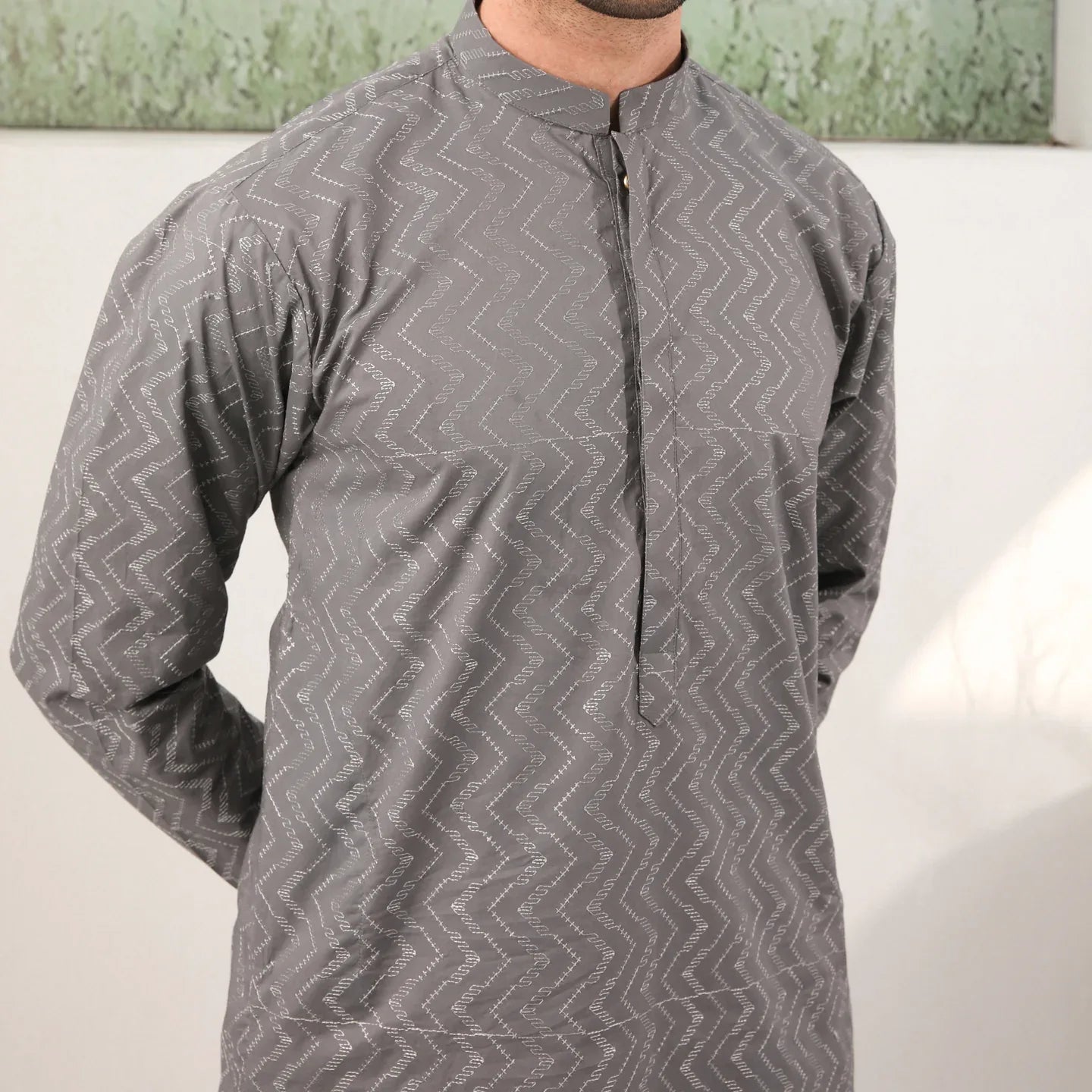A man wearing a light grey embroidered kurta with full sleeves and a mandarin collar, paired with a plain trouser.
