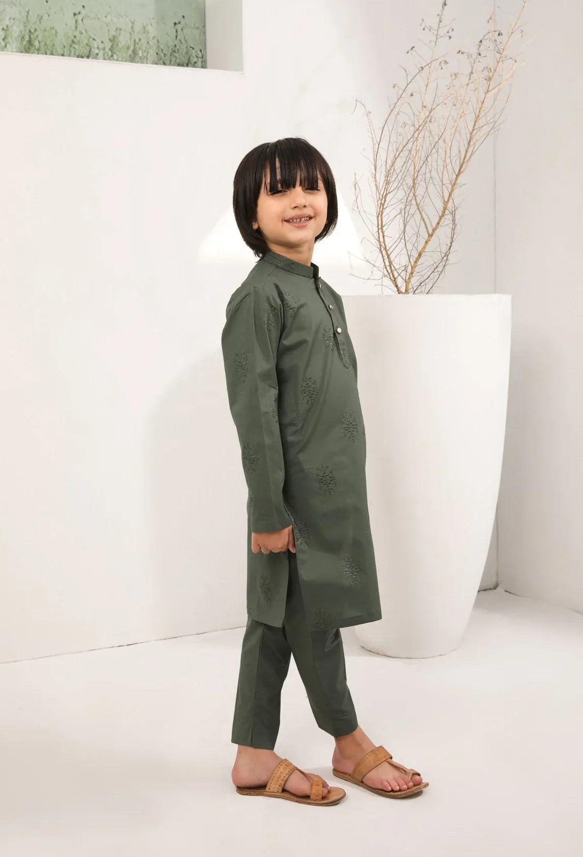 A child standing wearing an army green cotton embroidered kurta with full sleeves and a mandarin collar, paired with plain cotton trousers.