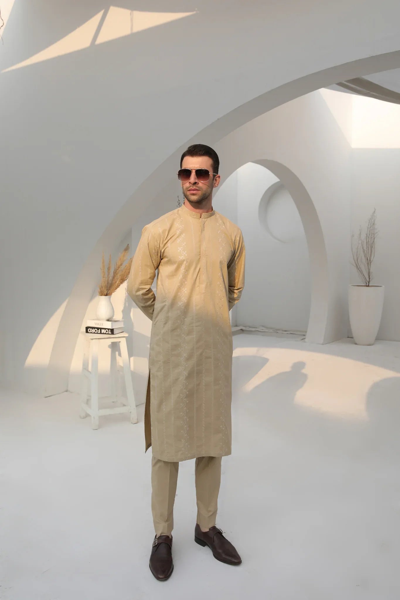 A man wearing a beige embroidered kurta with full sleeves and a mandarin collar, paired with a plain trouser.