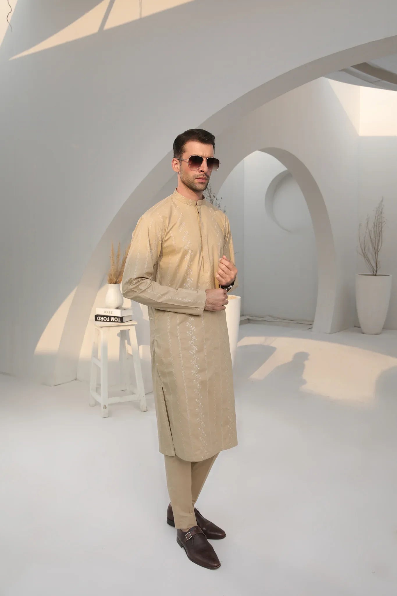 A man wearing a beige embroidered kurta with full sleeves and a mandarin collar, paired with a plain trouser.