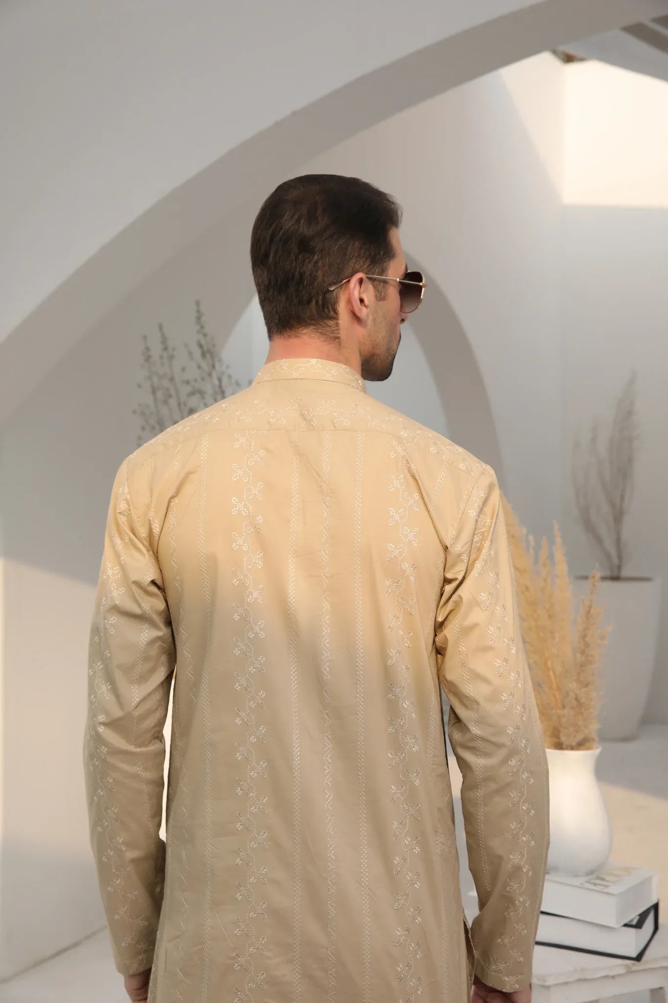 A man wearing a beige embroidered kurta with full sleeves and a mandarin collar, paired with a plain trouser.