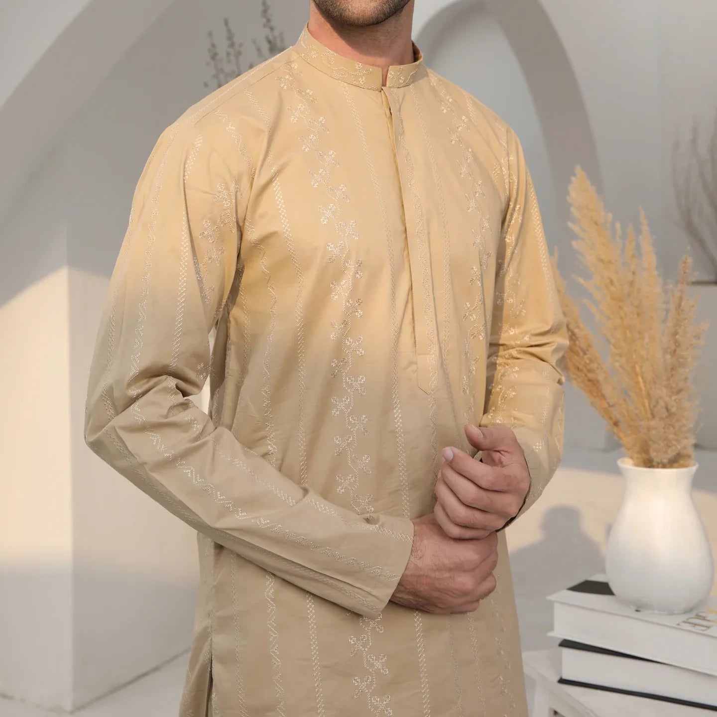 A man wearing a beige embroidered kurta with full sleeves and a mandarin collar, paired with a plain trouser.