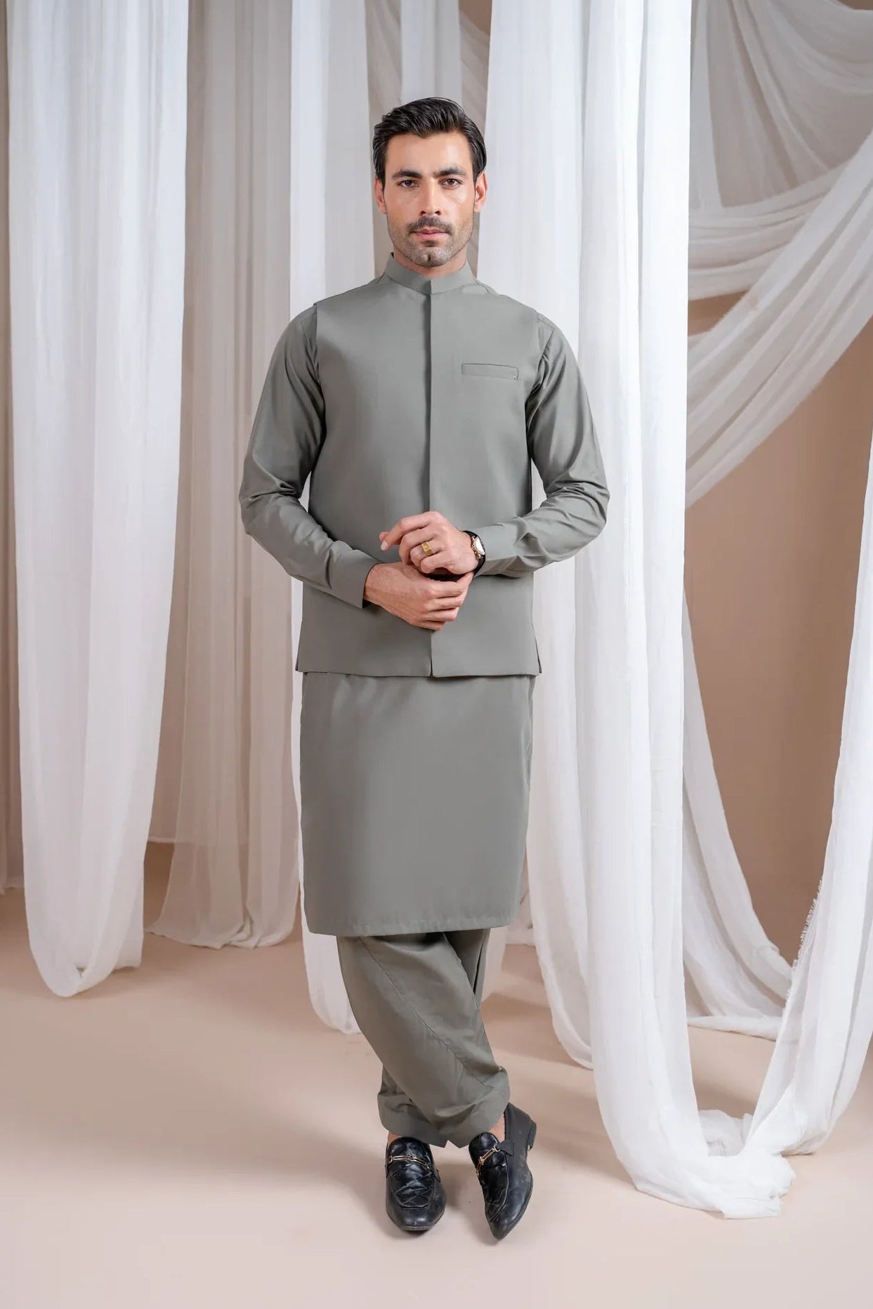 A man wearing a sand grey luxury formal Kameez Shalwar with a straight cut waistcoat and a patch pocket waistcoat.