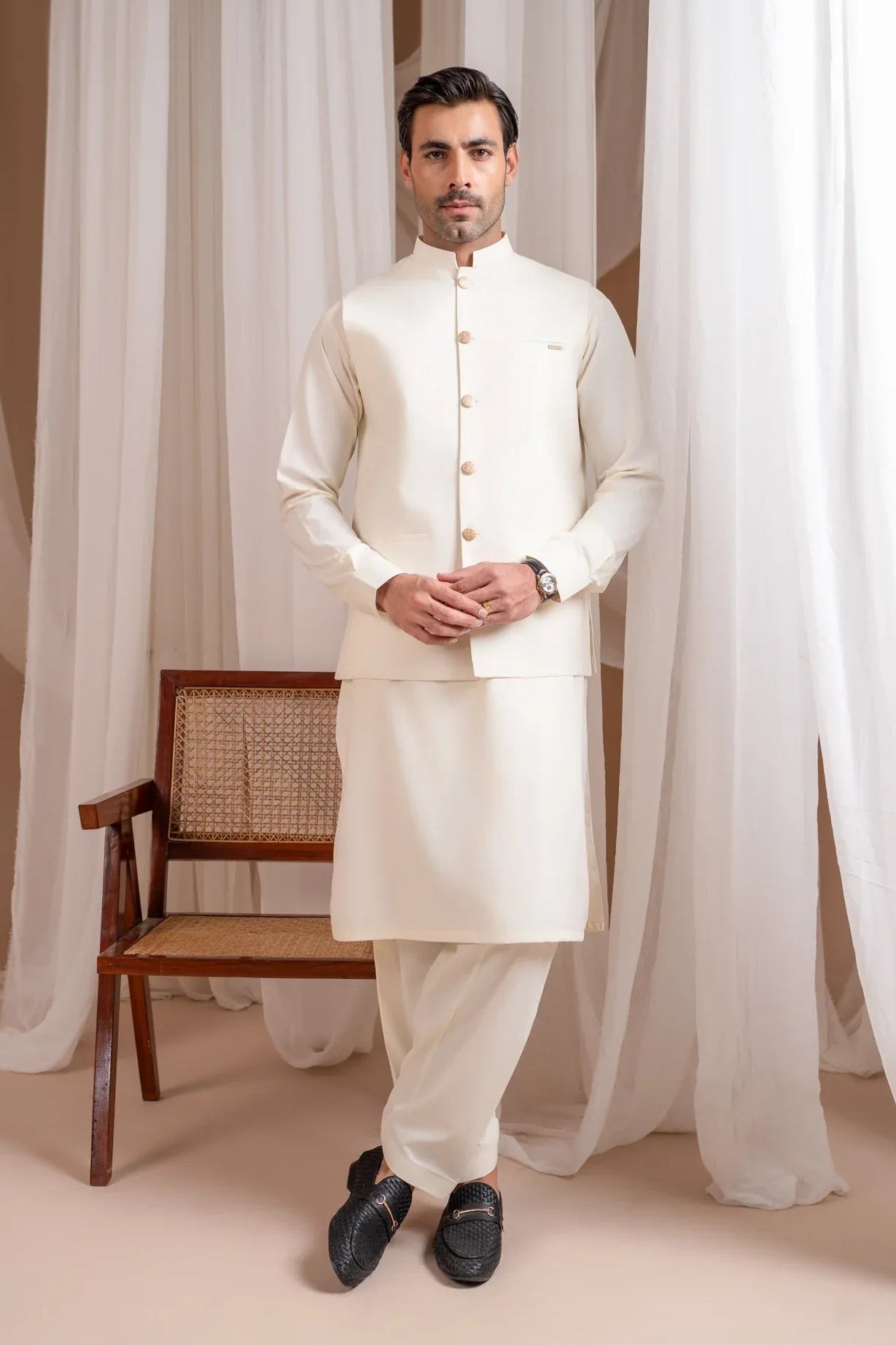 A man wearing a bosky white luxury formal kameez shalwar with a straight cut buttoned blended waistcoat.