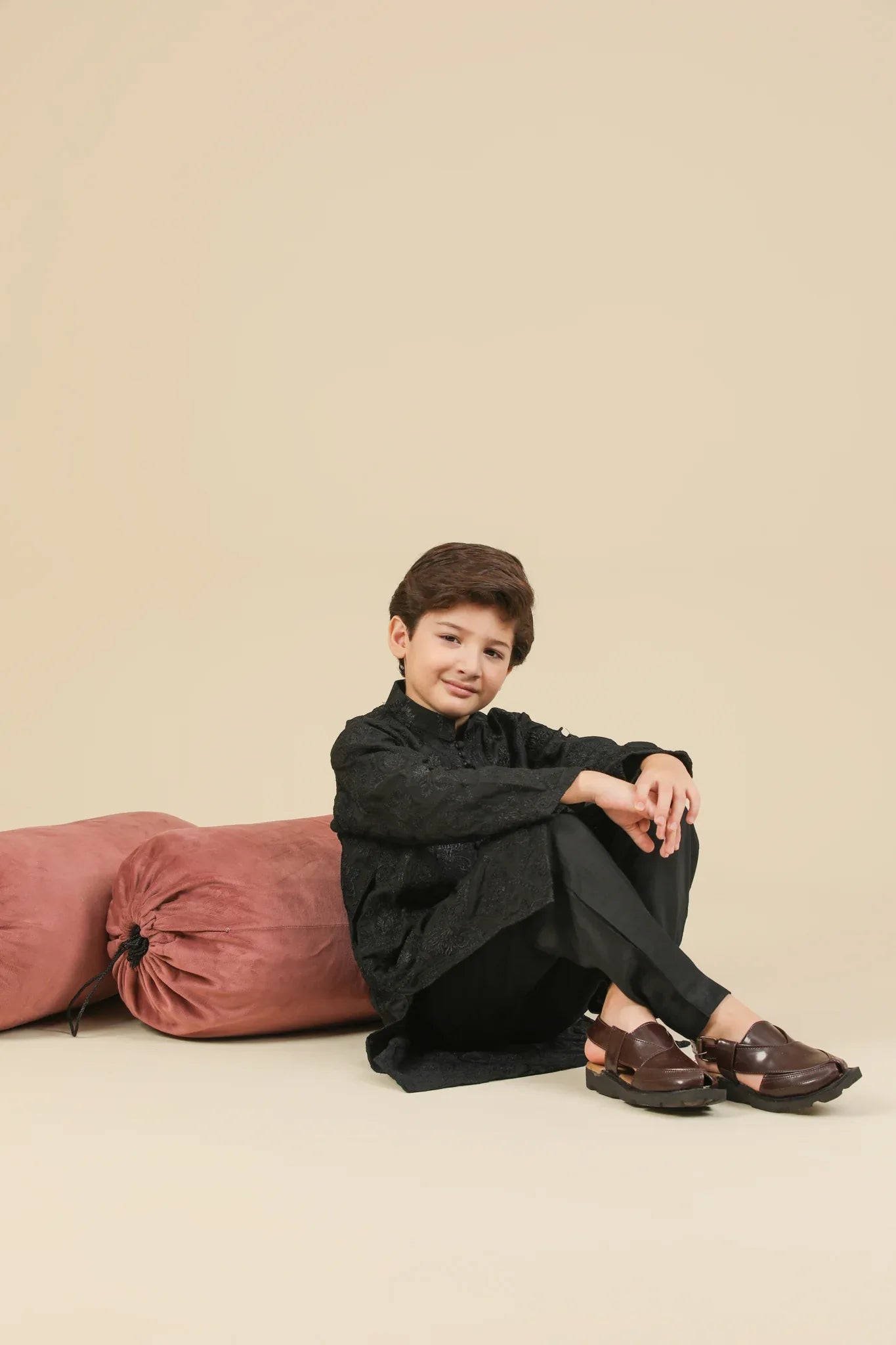 Young boy wearing a black raw silk embroidered kurta trouser outfit on a beige background