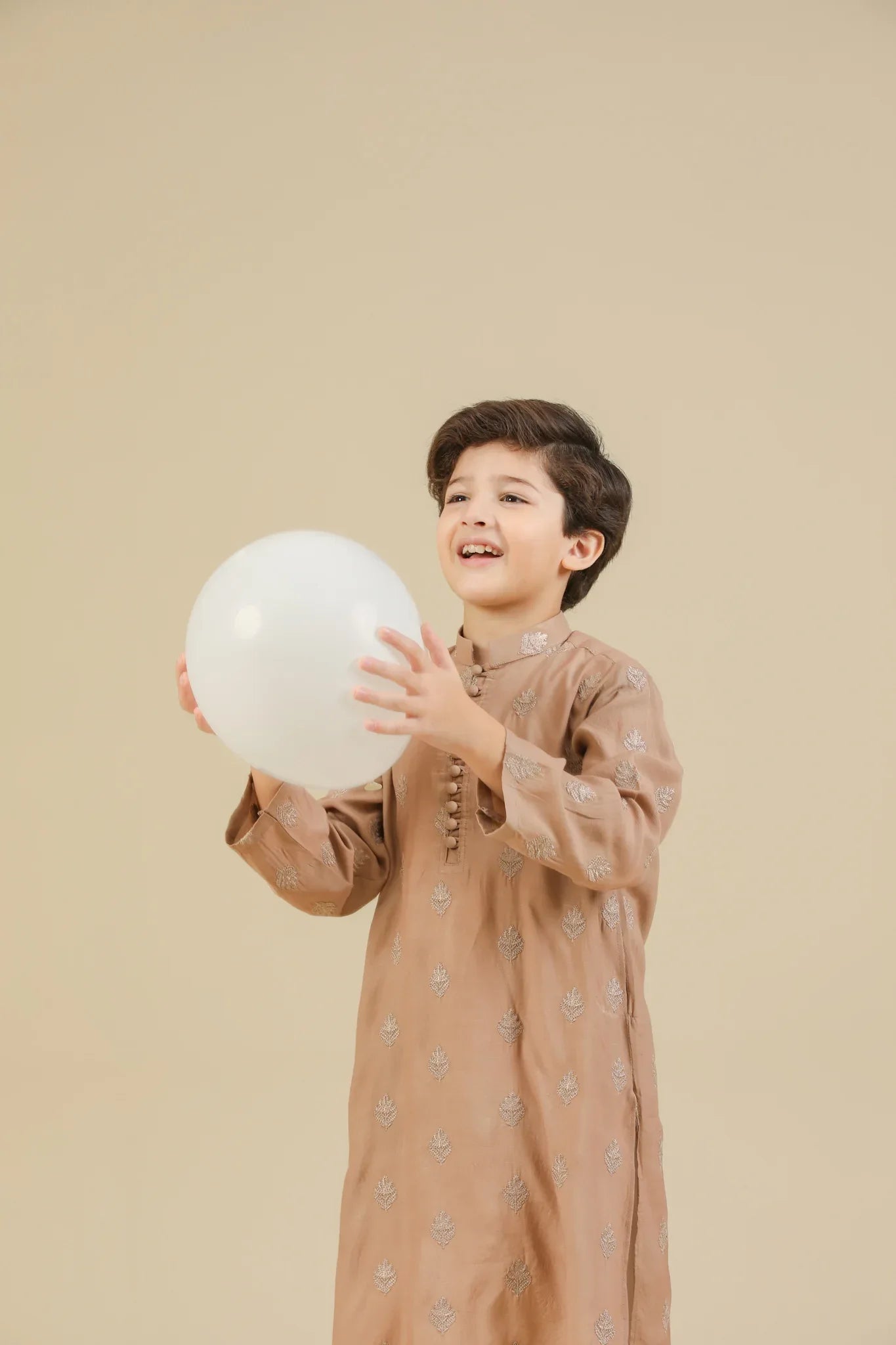 Young boy wearing a peach raw silk embroidered kurta with white trouser on a beige background
