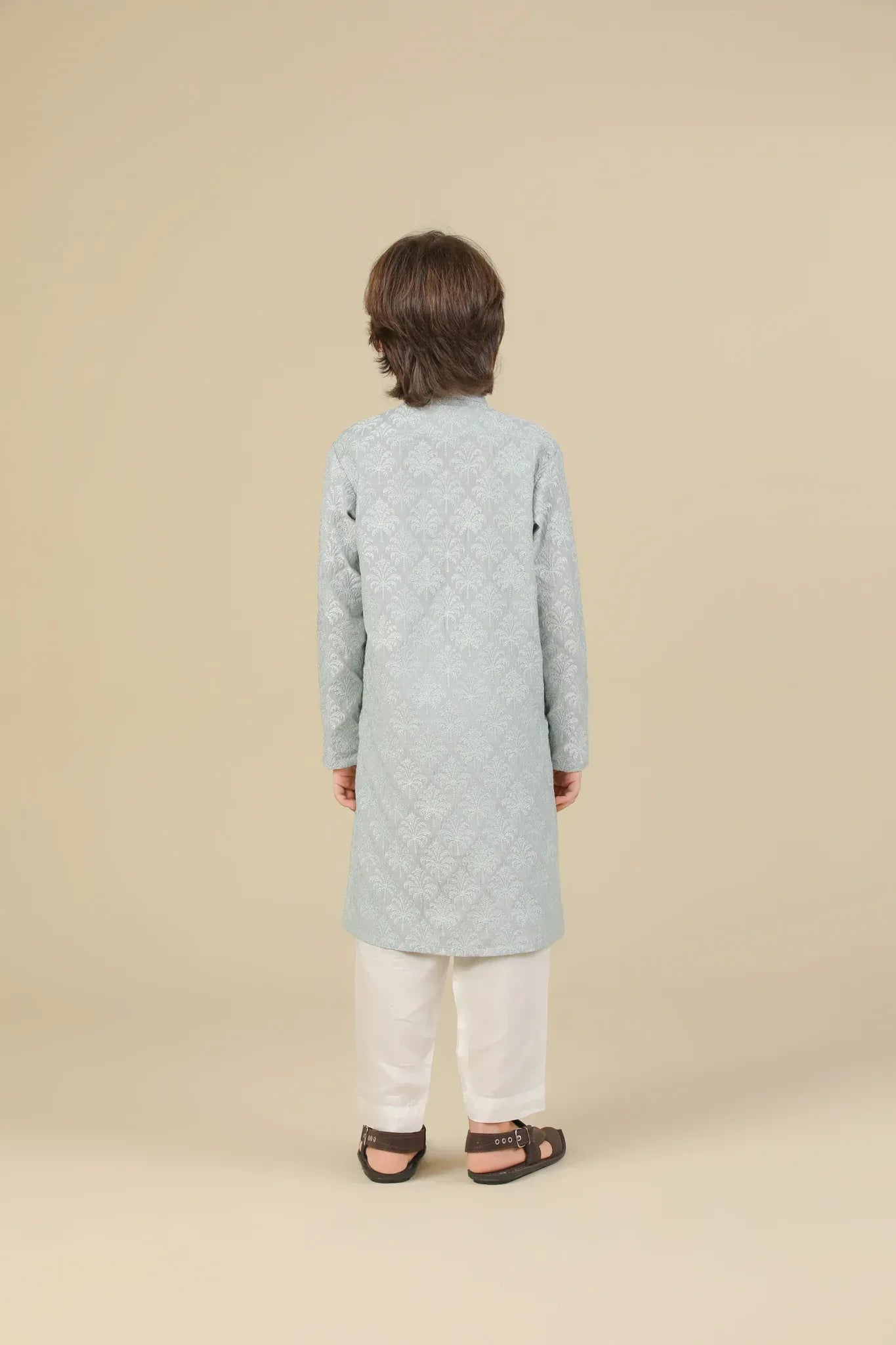 Young boy wearing an ice blue embroidered kurta with white pajama on a beige background