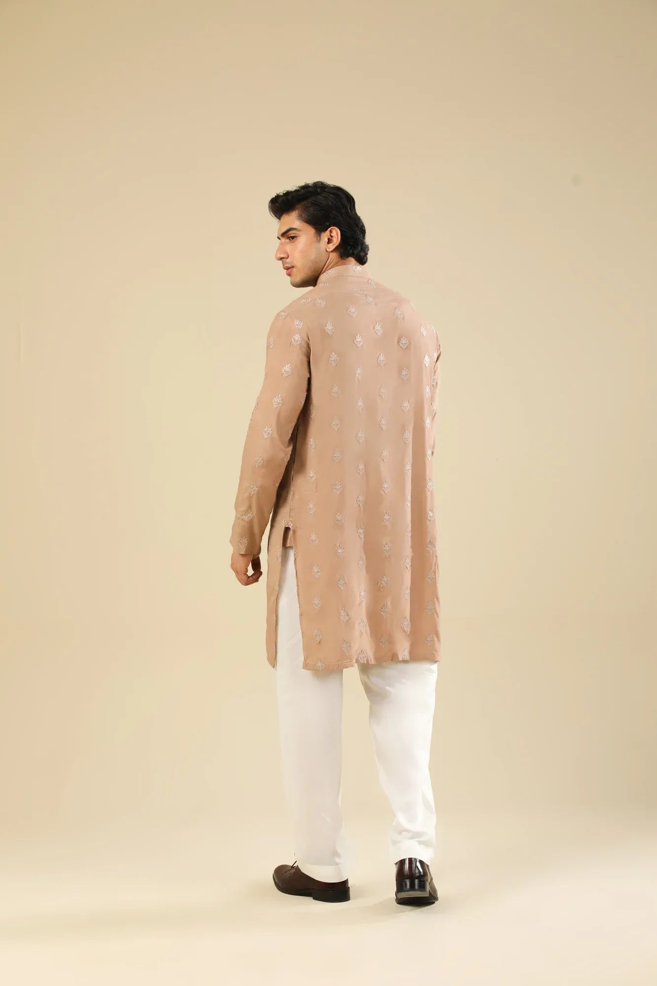 Man wearing a peach embroidered kurta and white trouser with a beige background