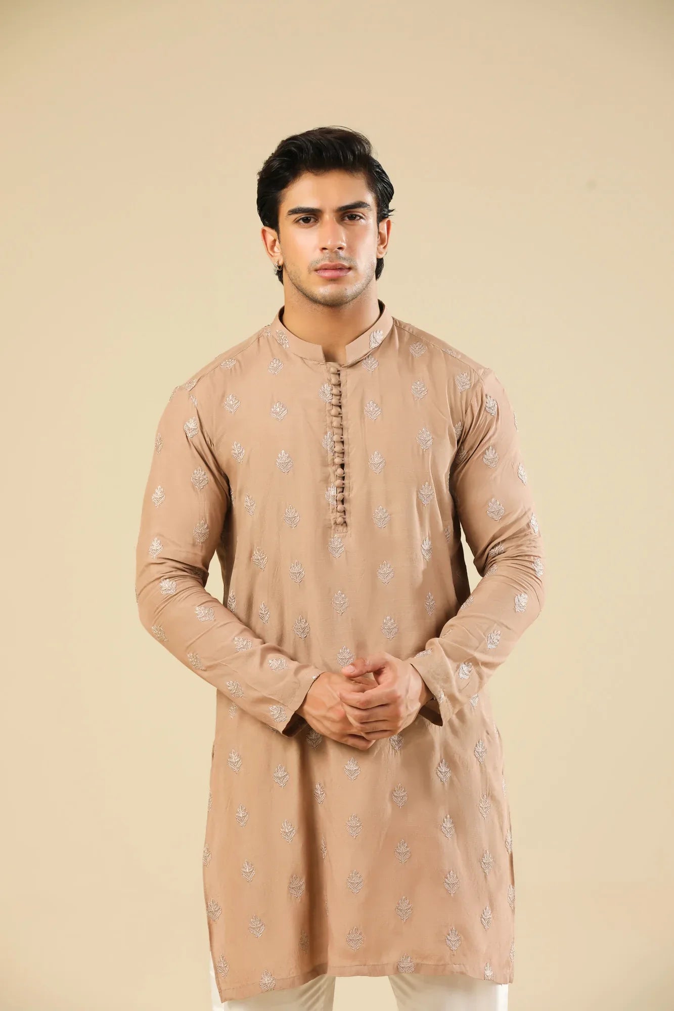 Man wearing a peach embroidered kurta and white trouser with a beige background