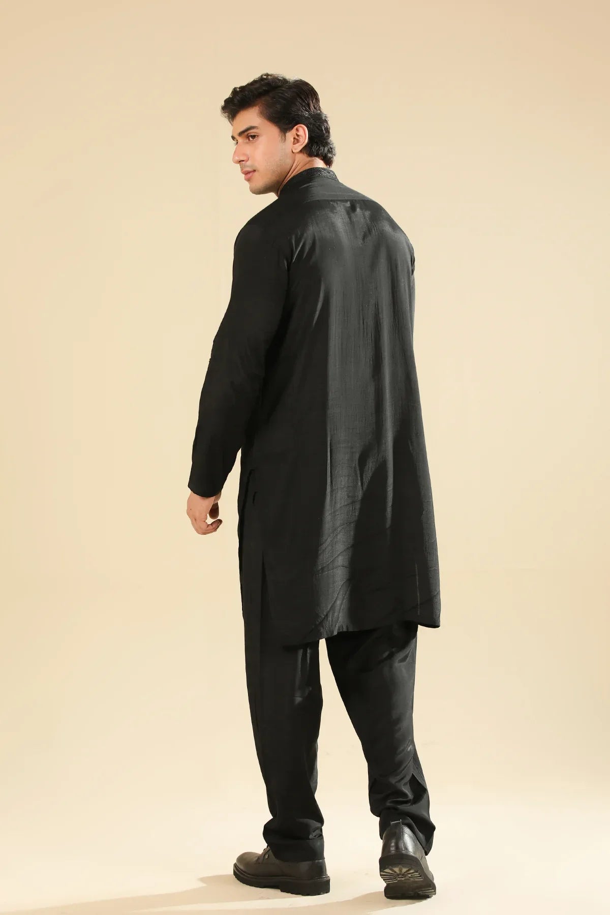 Man wearing a black raw silk embroidered kurta trouser against a beige background