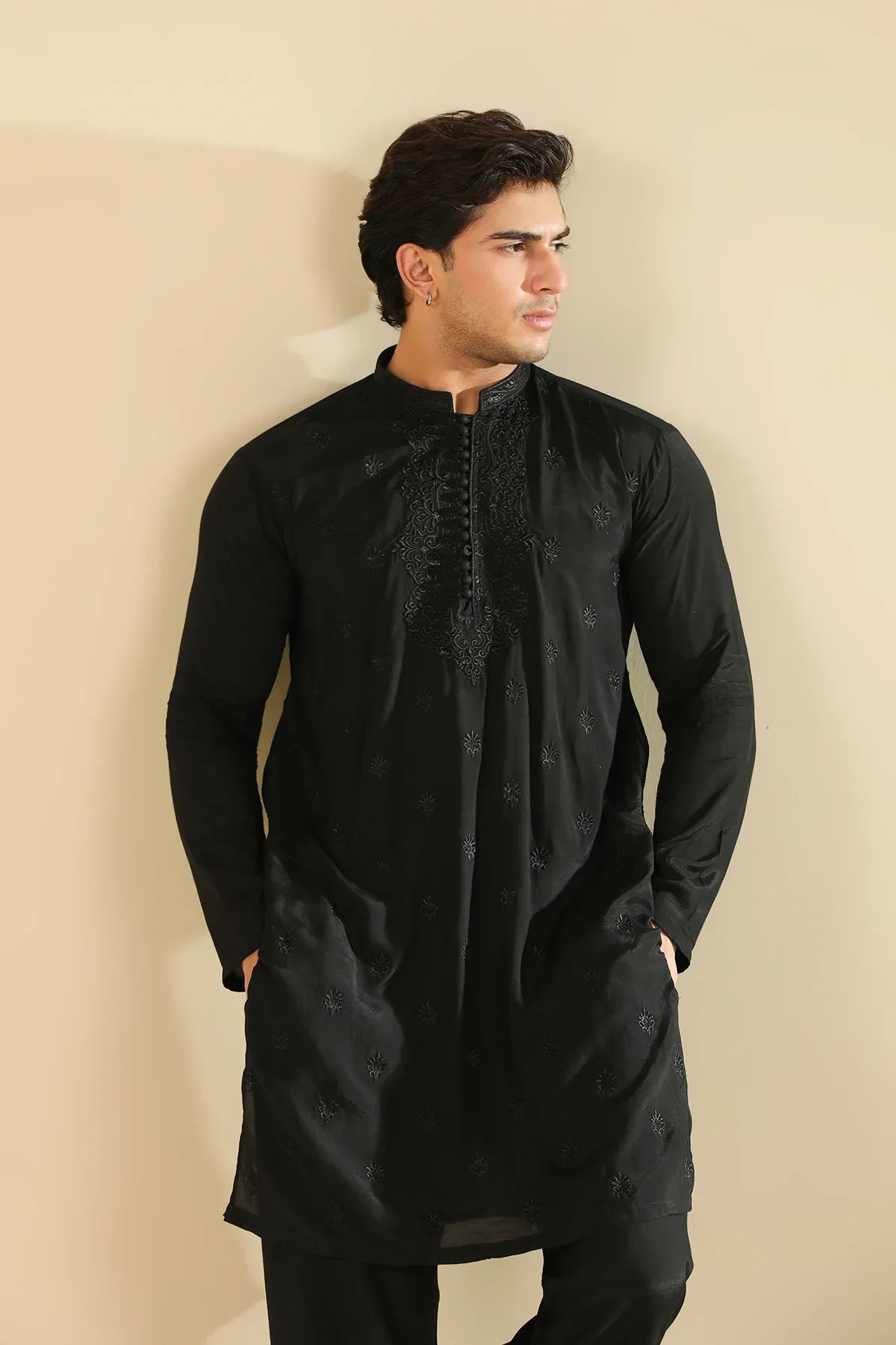 Man wearing a black raw silk embroidered kurta trouser against a beige background